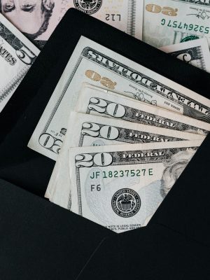 From above of dollar bills in opened black envelope placed on stack of United states cash money as concept of personal income