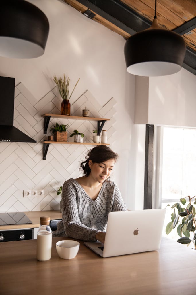 Young woman in cozy kitchen using laptop. Bright, daylight settings for remote work or study.